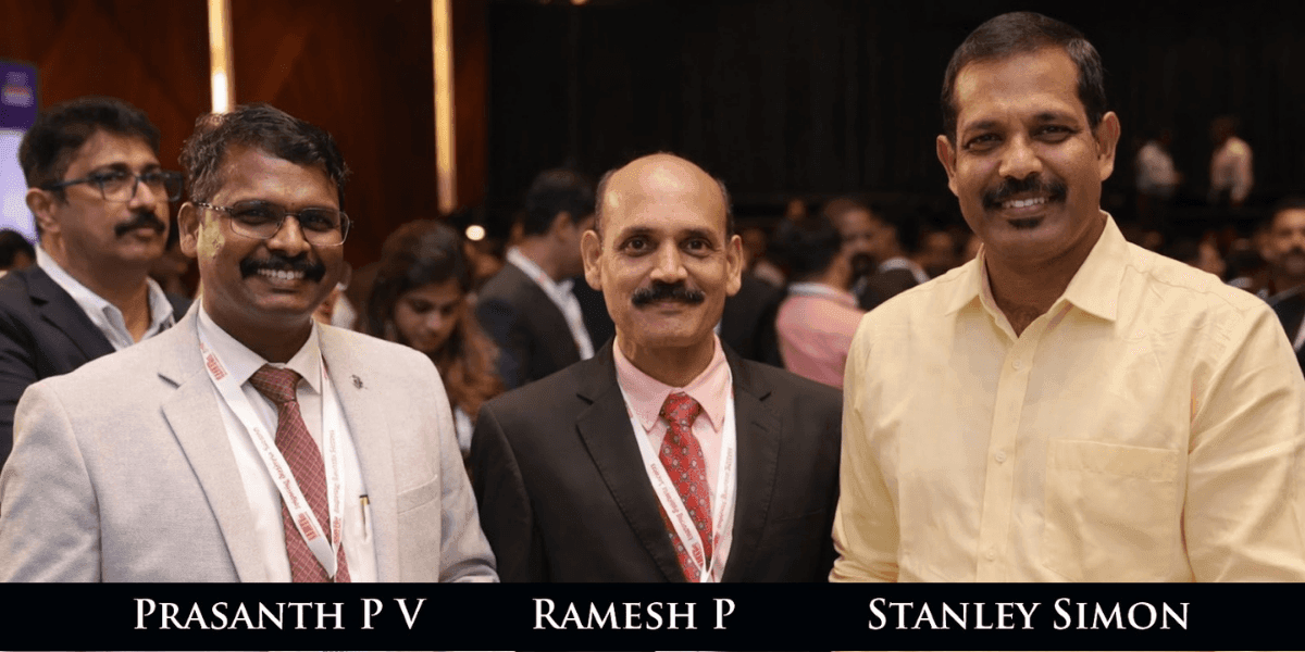 Three men in business attire stand smiling at an event. They are in a crowded room with blurred figures in the background, conveying a professional and friendly atmosphere.
