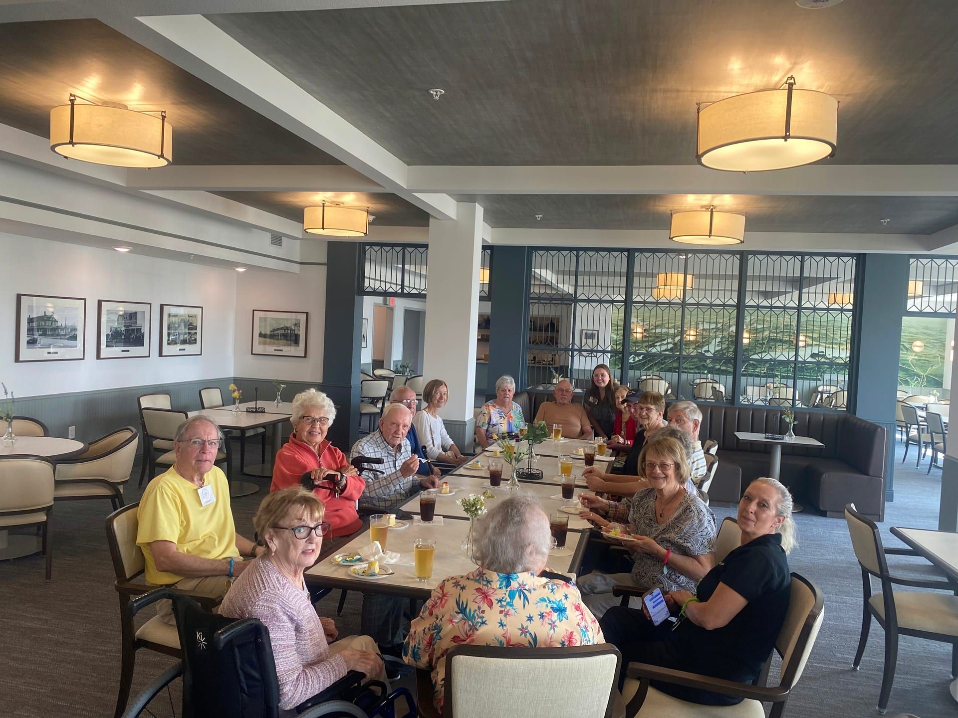 A group of elderly individuals enjoying a meal together at a bright and spacious dining area, with tables set up in a comfortable and welcoming atmosphere.