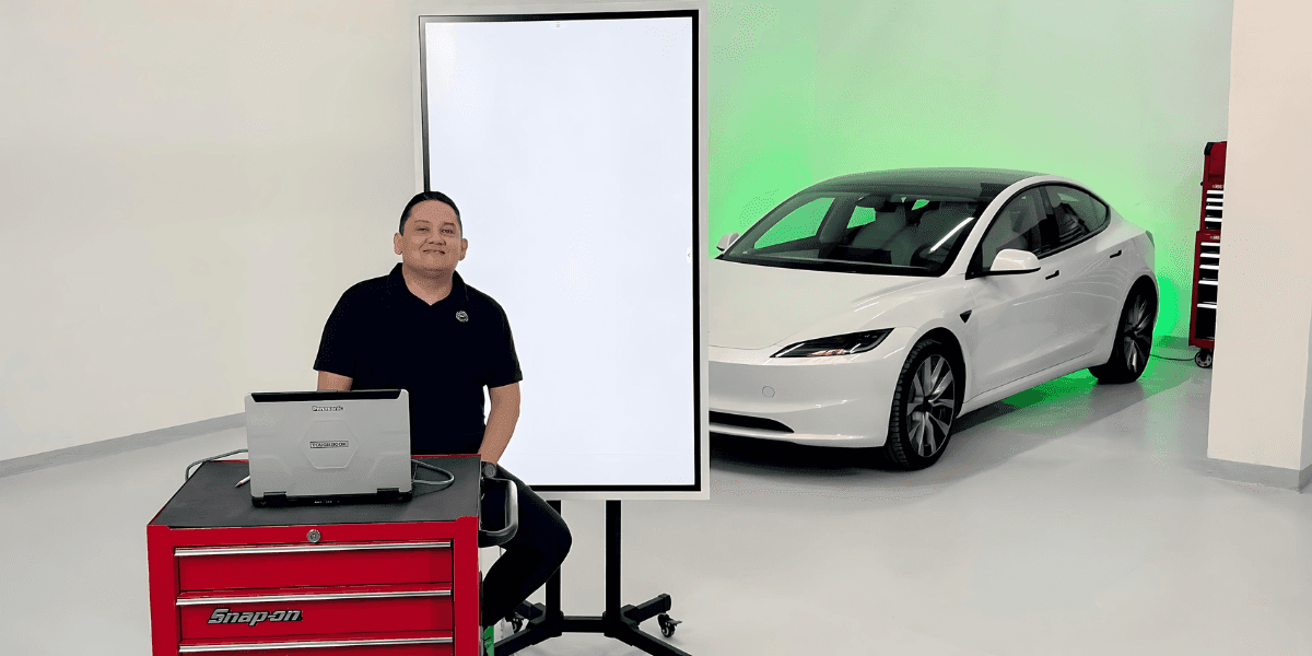 A person standing in a garage with a white Tesla car, a laptop, and a Snap-on tool chest.