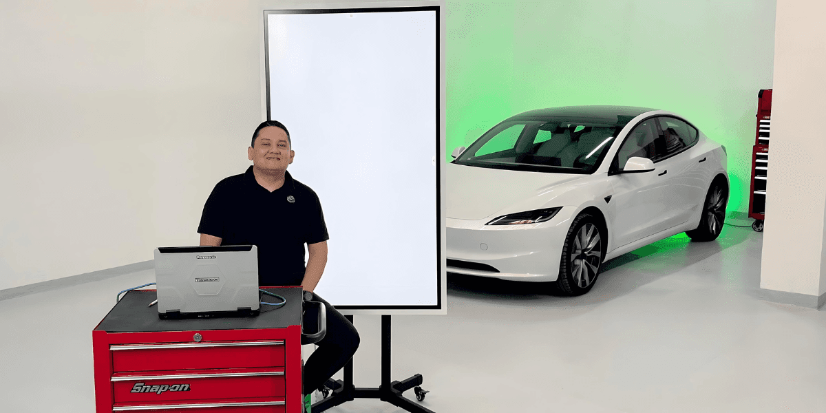 A person standing in a garage with a white Tesla car, a laptop, and a Snap-on tool chest.