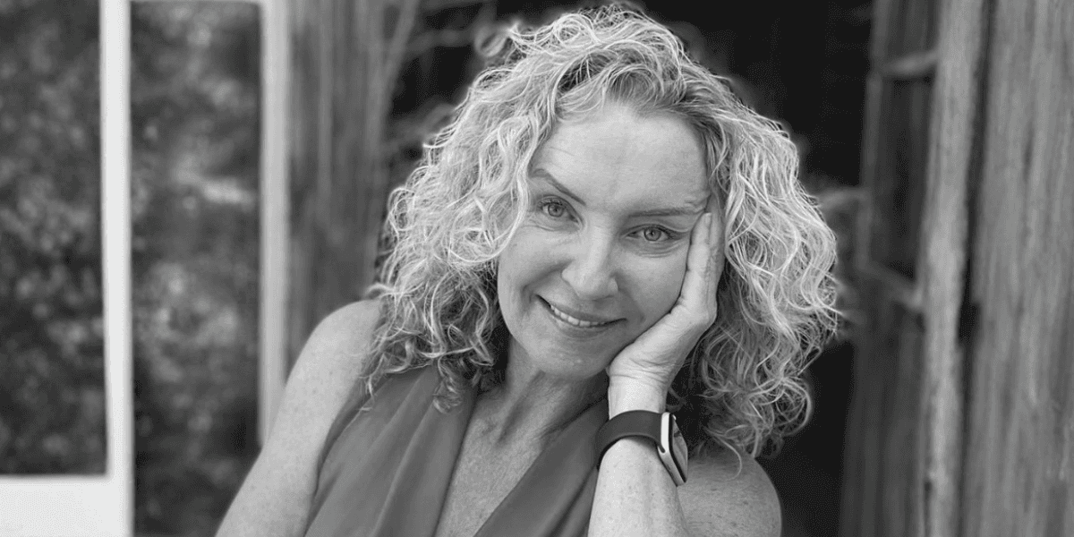 Black-and-white portrait of Sarah Lucas smiling with hand resting on her face outdoors.