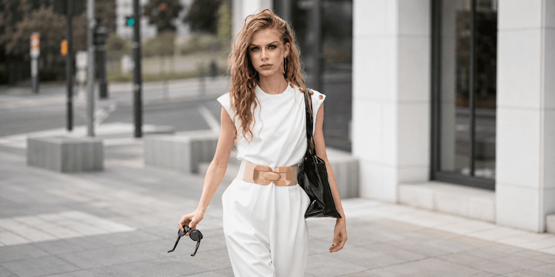 Nelly Opitz walks outdoors in a white belted outfit carrying a black handbag.
