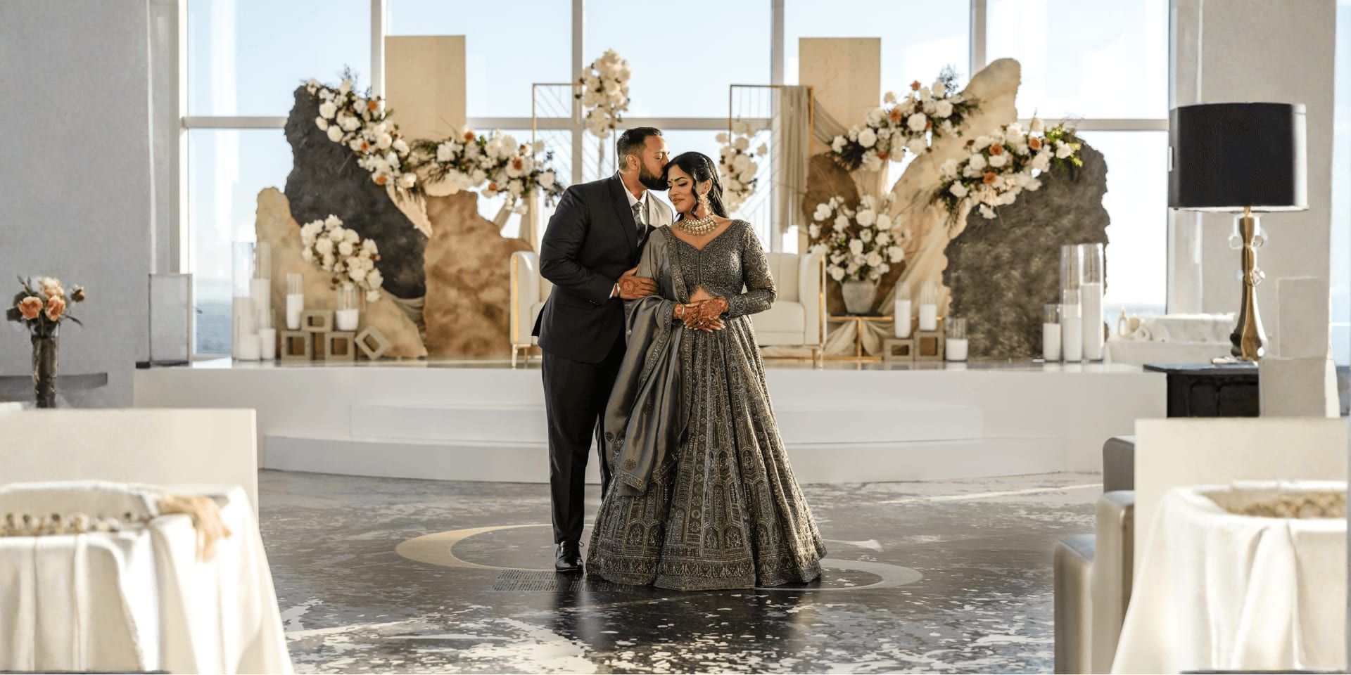 Couple poses before elegant floral wedding stage designed by Onyx Moon Events during luxury indoor celebration.