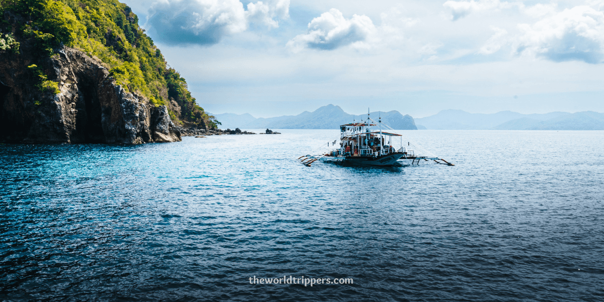 A boat sailing in clear turquoise waters near lush islands, part of the scenic Coron to El Nido expedition.