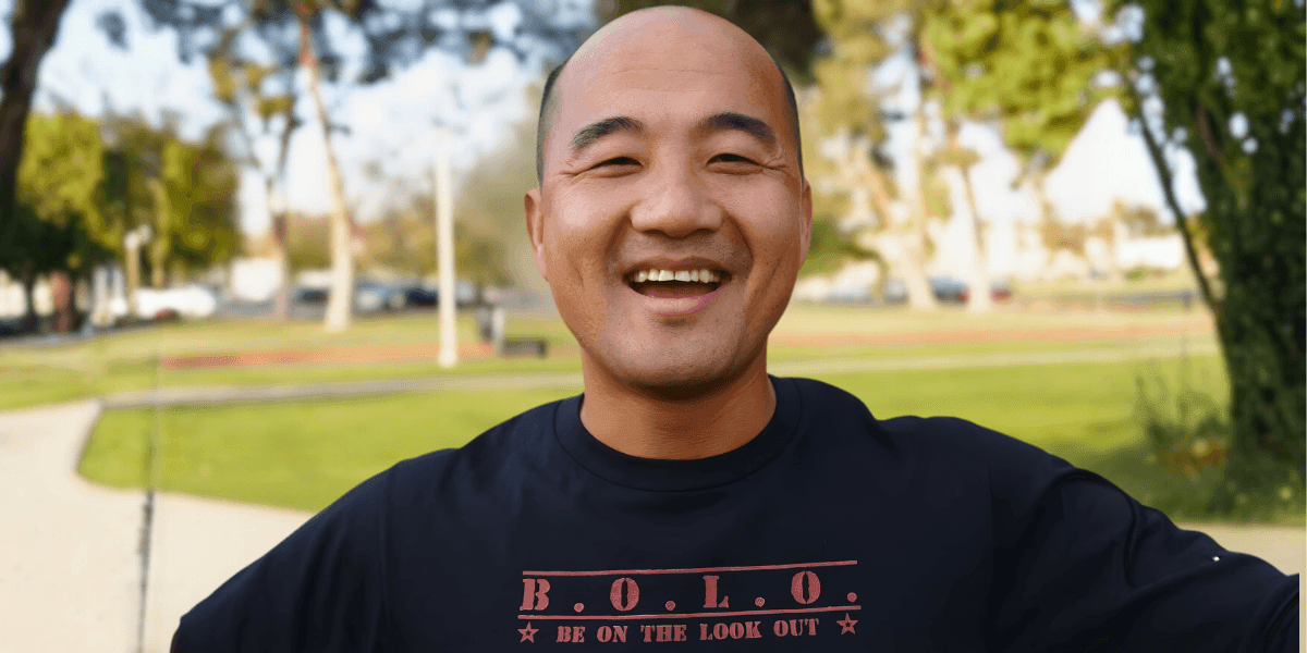 Kao Lee smiling outdoors, wearing a B.O.L.O. shirt, embodying the journey of self-discovery and service through his memoir.