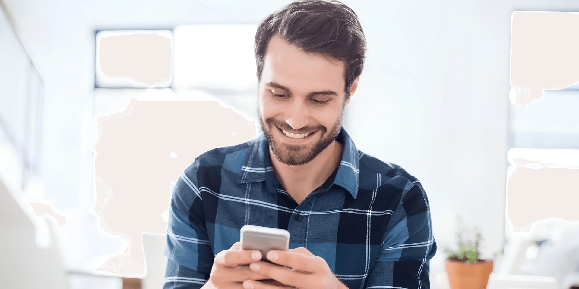Man smiles while using a smartphone indoors.