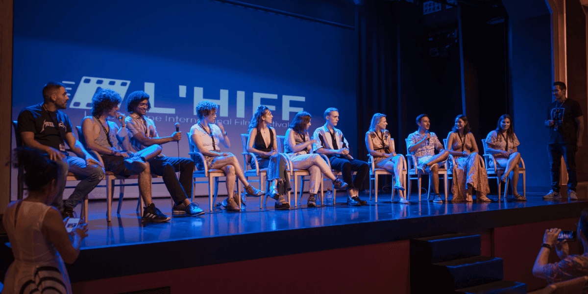 "A panel discussion at the L'HIFF (Los Angeles International Film Festival) with a group of individuals seated on stage, engaging in conversation, under a blue-lit backdrop with the festival logo visible."