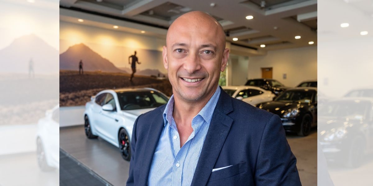 Portrait of Warren Foyn, founder of NextGen Motor Academy, standing confidently in a modern car showroom with luxury vehicles.