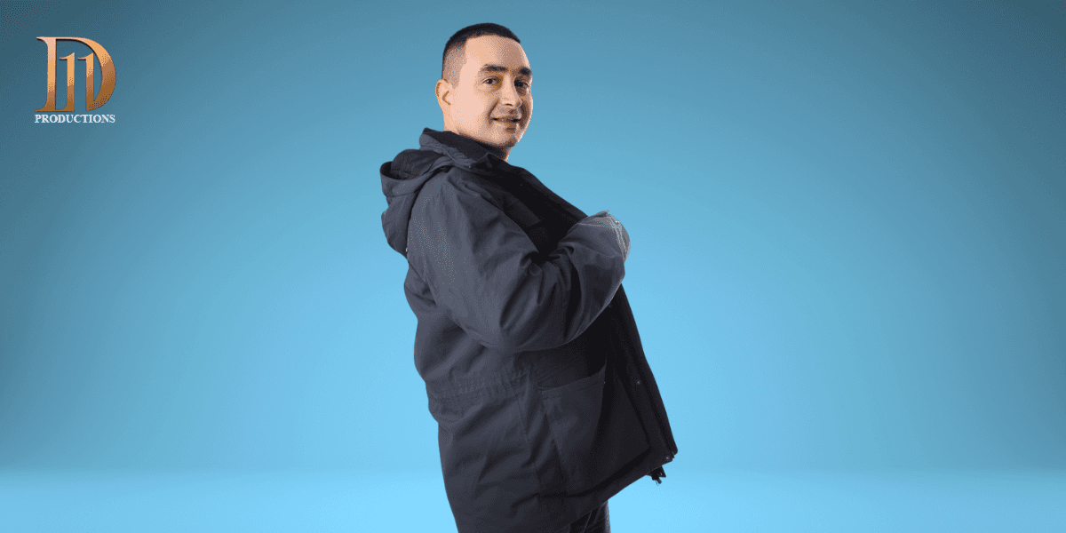 Man in dark jacket poses confidently against blue background with 11D Productions logo.