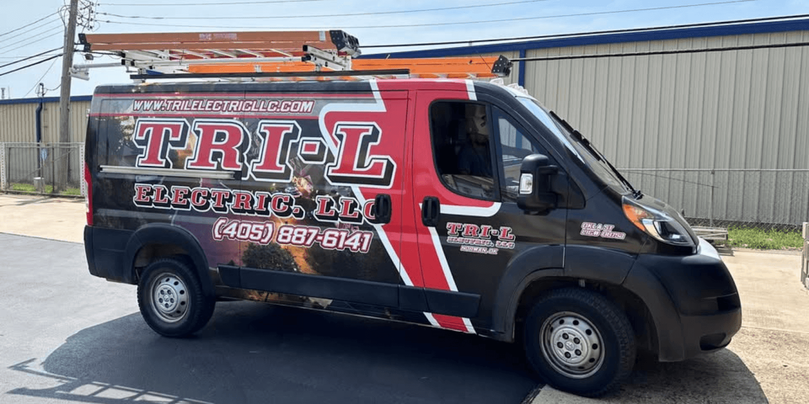 Tri-L Electric service van parked outside an industrial building with ladders mounted on top.