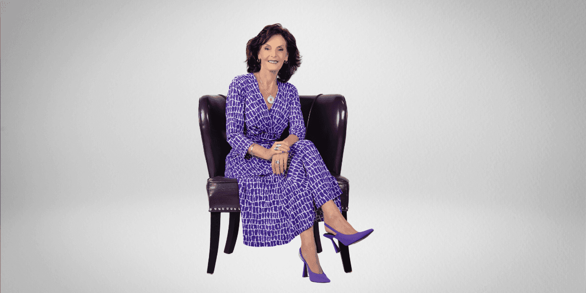 Dr. Carol Talbot, a transformative speaker and author, sitting confidently in a purple dress and heels, in a chair.