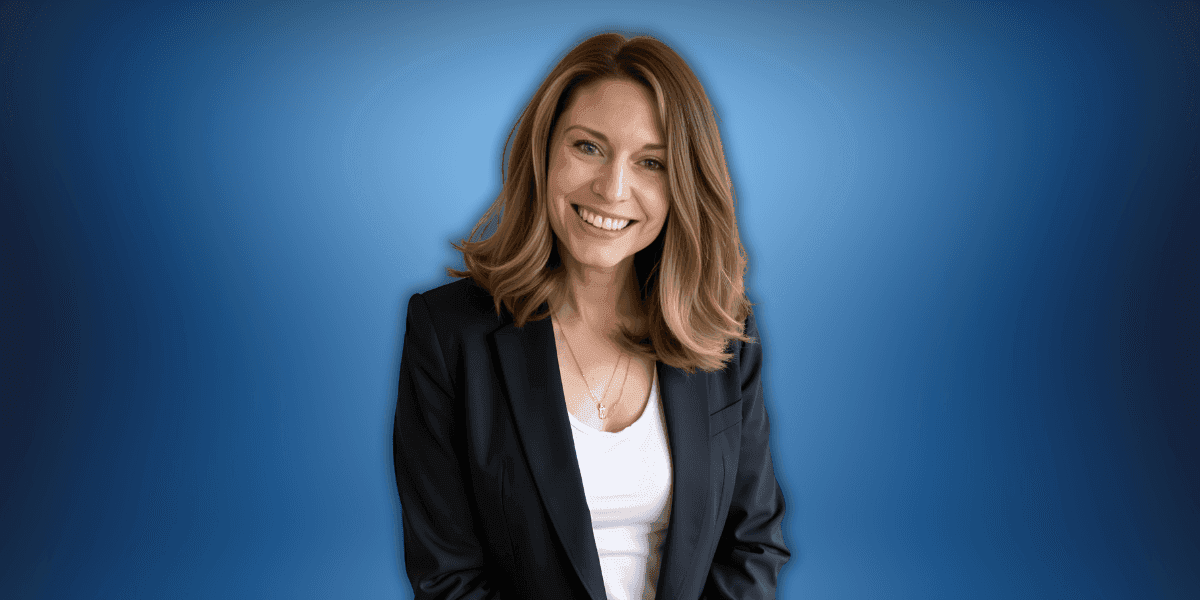 Professional woman smiling in a black blazer with a blue background, representing confidence and success in business.