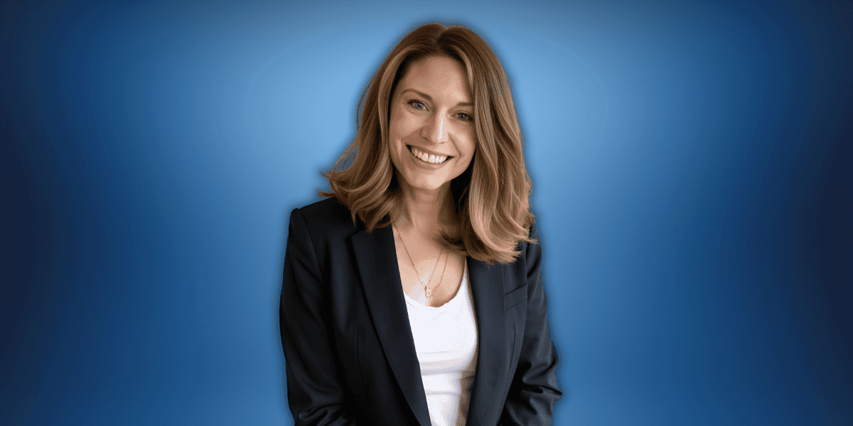 Professional woman smiling in a black blazer with a blue background, representing confidence and success in business.