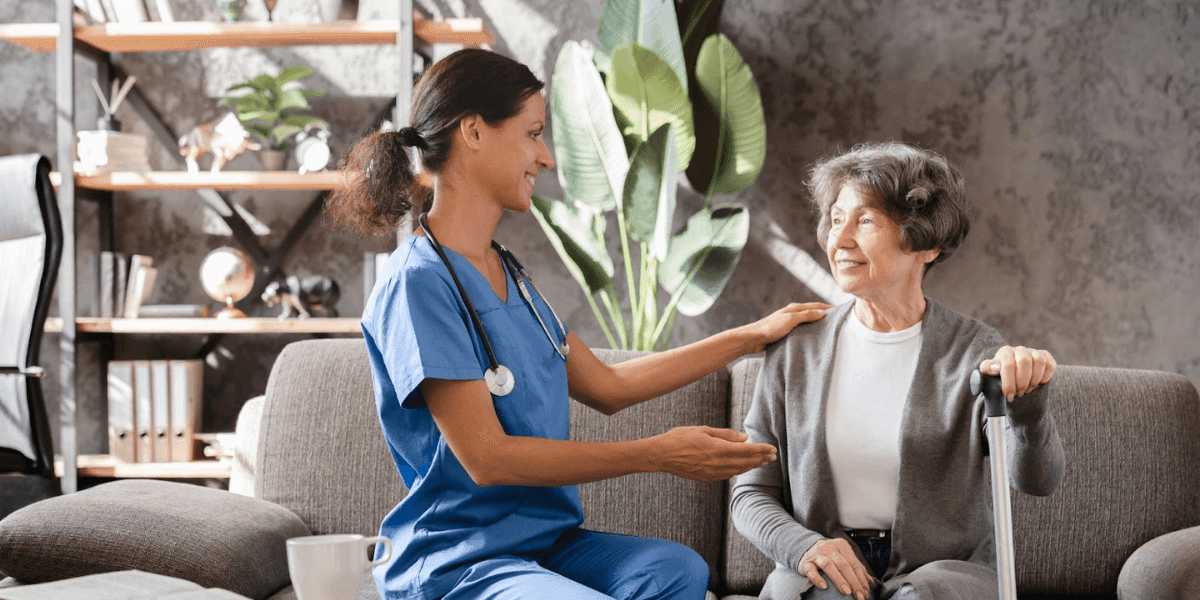 Image ALT Text Generator said: Smiling senior woman chatting with caregiver in a bright common room, representing the choice between day care and assisted living.