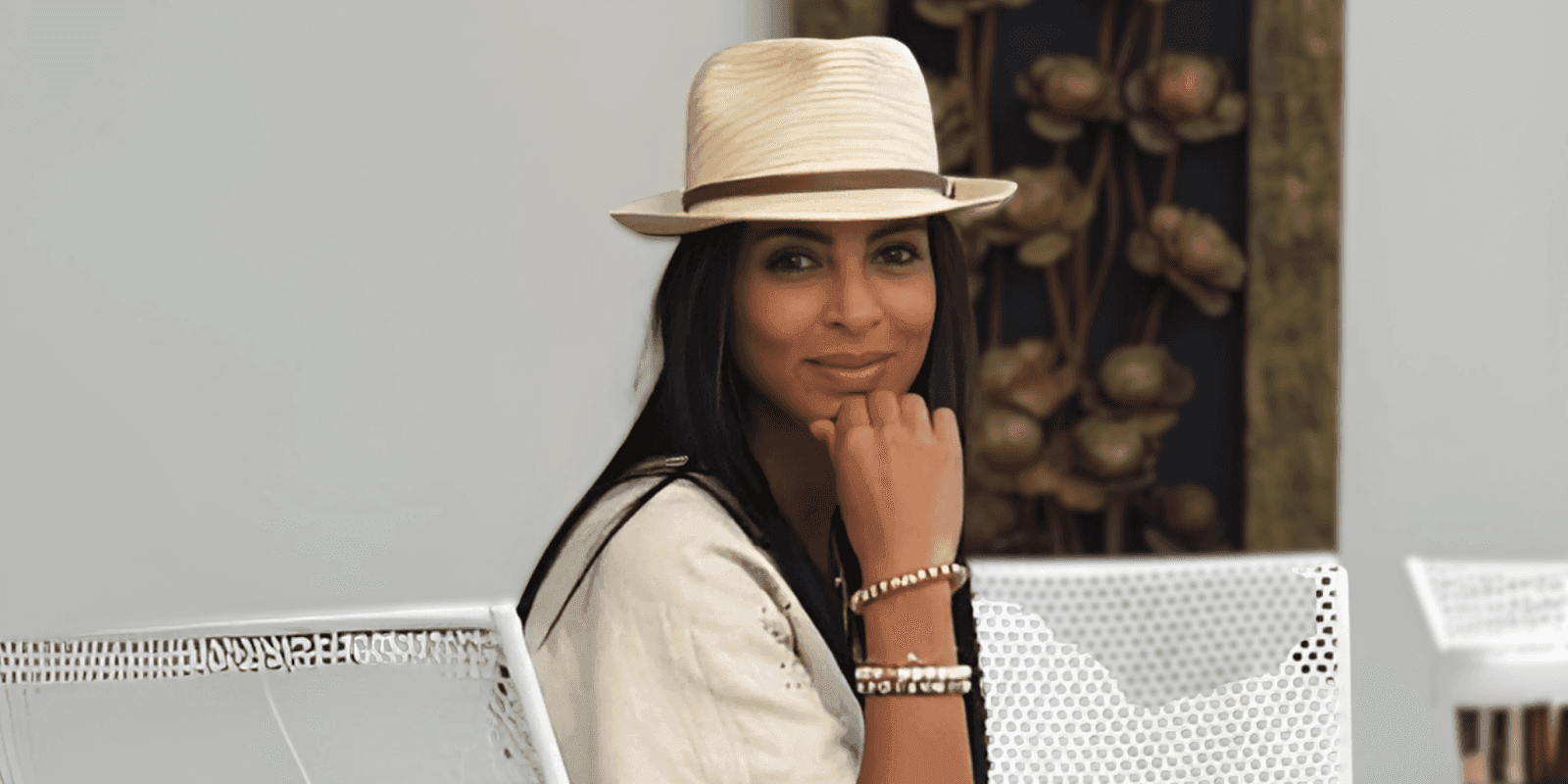 "A woman wearing a black dress and a wide-brimmed hat, standing outdoors with a natural landscape background, promoting Murun Pearls jewelry."
