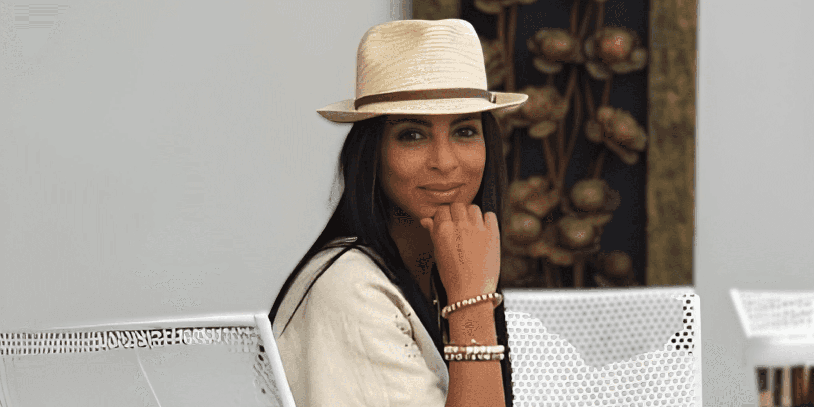 "A woman wearing a black dress and a wide-brimmed hat, standing outdoors with a natural landscape background, promoting Murun Pearls jewelry."