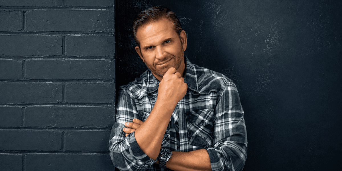 Angelo Oddo poses in a plaid shirt against a dark wall.