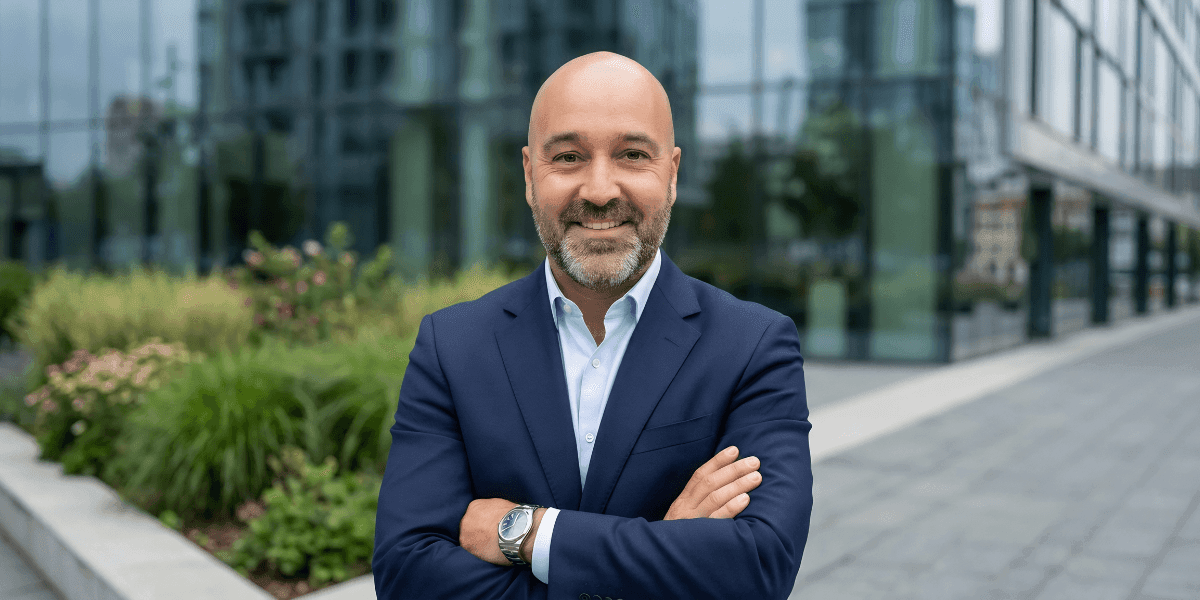 Smiling businessman in navy suit standing outdoors near modern office buildings.