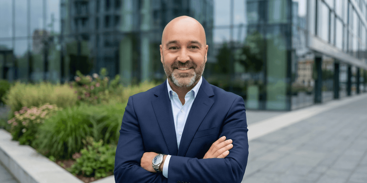 Smiling businessman in navy suit standing outdoors near modern office buildings.