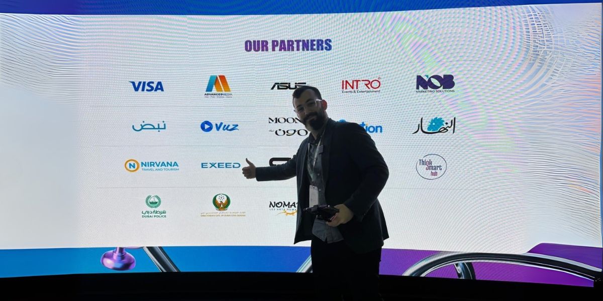 Individual standing in front of a screen with partner logos including Visa, Advance Media, Nirvana Travel, and Dubai Police at an event, promoting Accorres Consultancy House's corporate partnerships