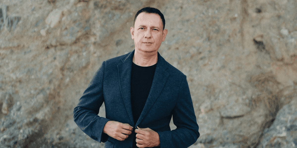 "Author Severino Ricci standing confidently in front of a rocky background, dressed in a casual yet sophisticated blazer, exuding a professional and thoughtful presence."