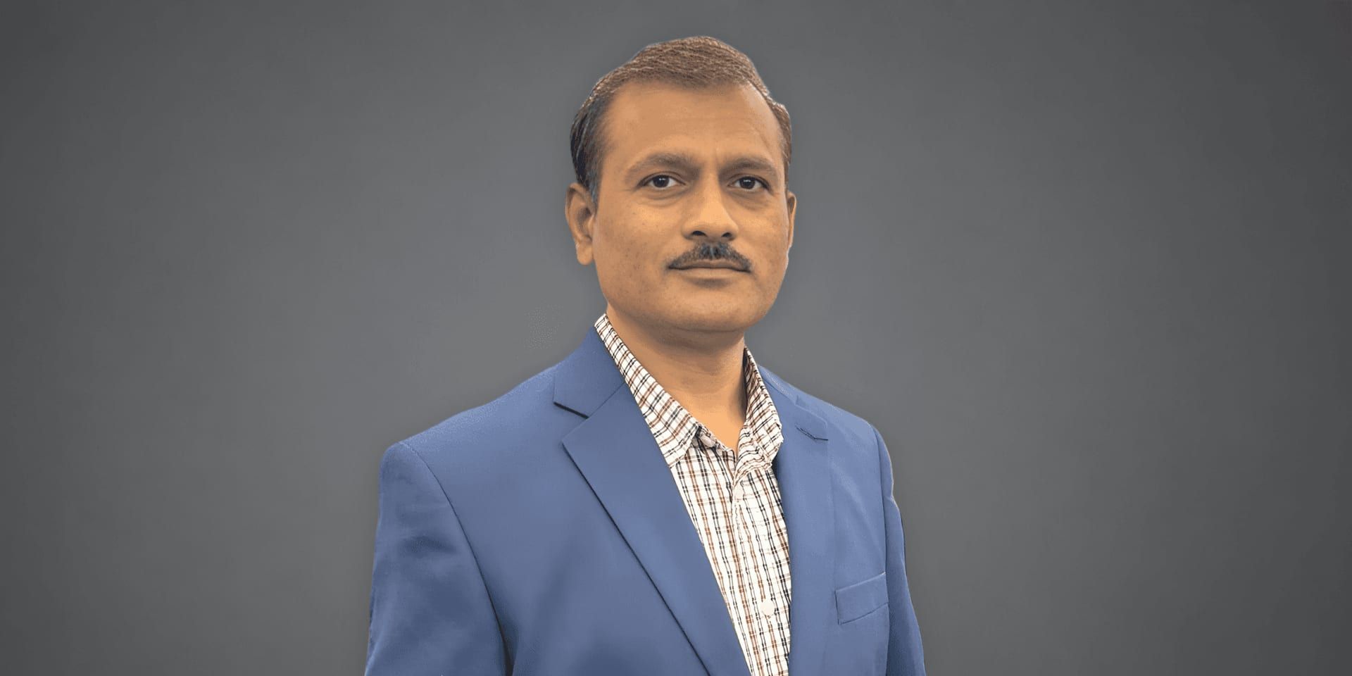 Pradip Thorat wearing a blue blazer and checkered shirt in a professional portrait against a gray background.