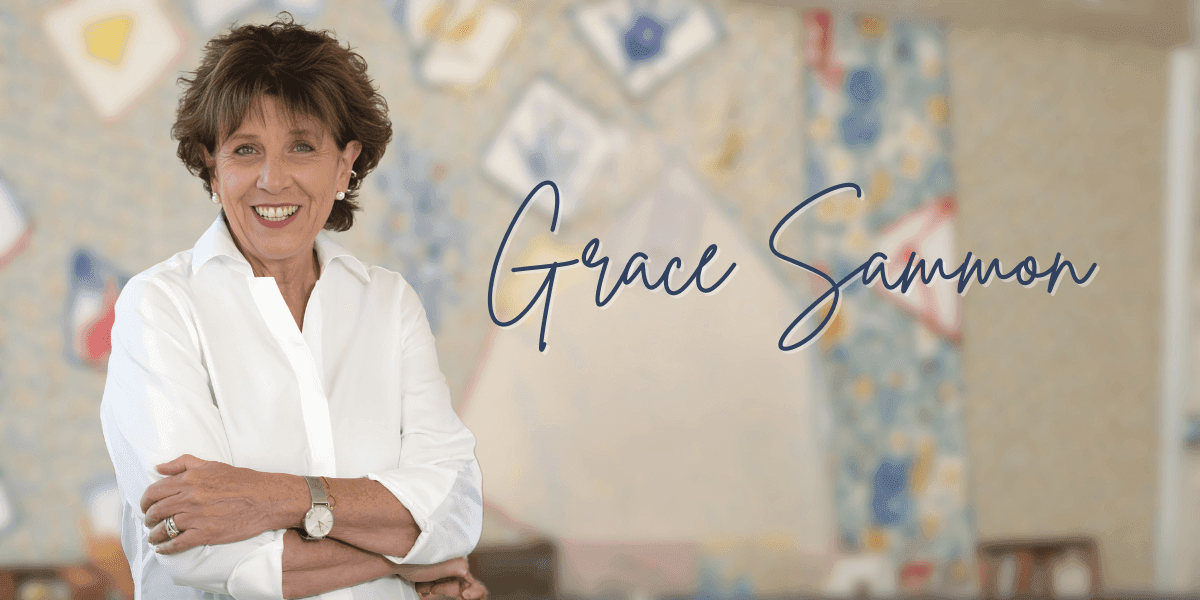 Smiling woman in a white blouse stands with arms crossed against a blurred quilt-patterned background; elegant script reads "Grace Sammon."