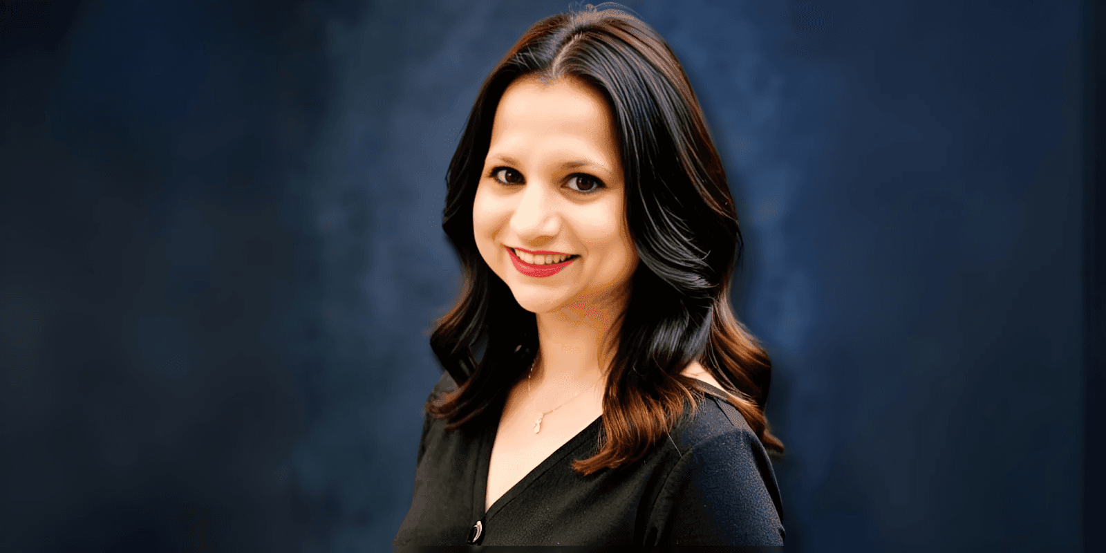 Portrait of a smiling woman with long hair, wearing a black blouse, set against a dark blue background, radiating confidence and warmth.