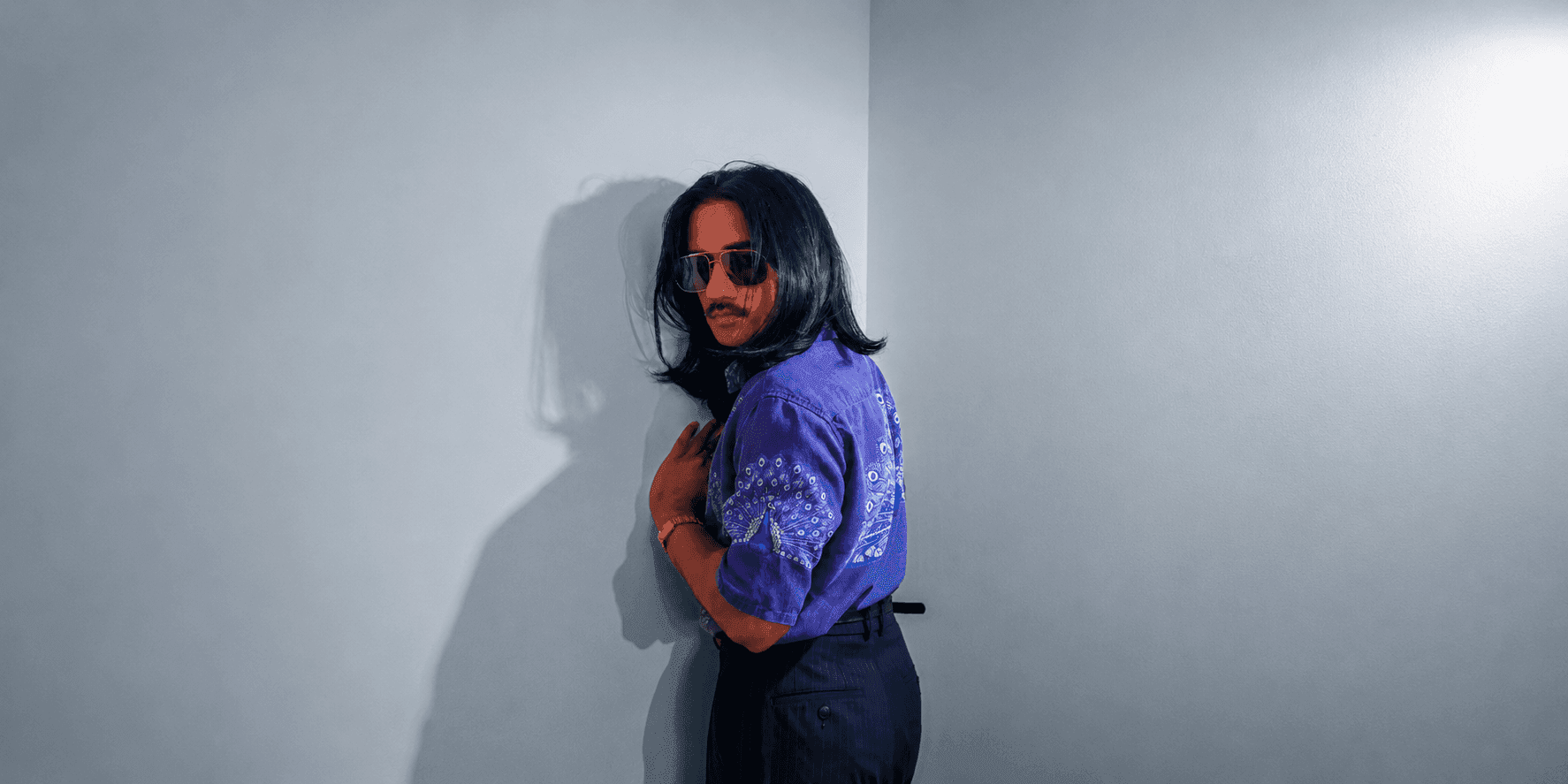 Person wearing a purple embroidered shirt and sunglasses, standing against a light-colored wall.