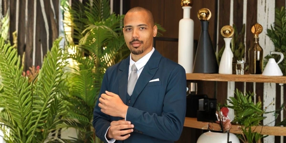 Wilme Ulasia dressed in a tailored suit, presenting a professional image amidst lush greenery.