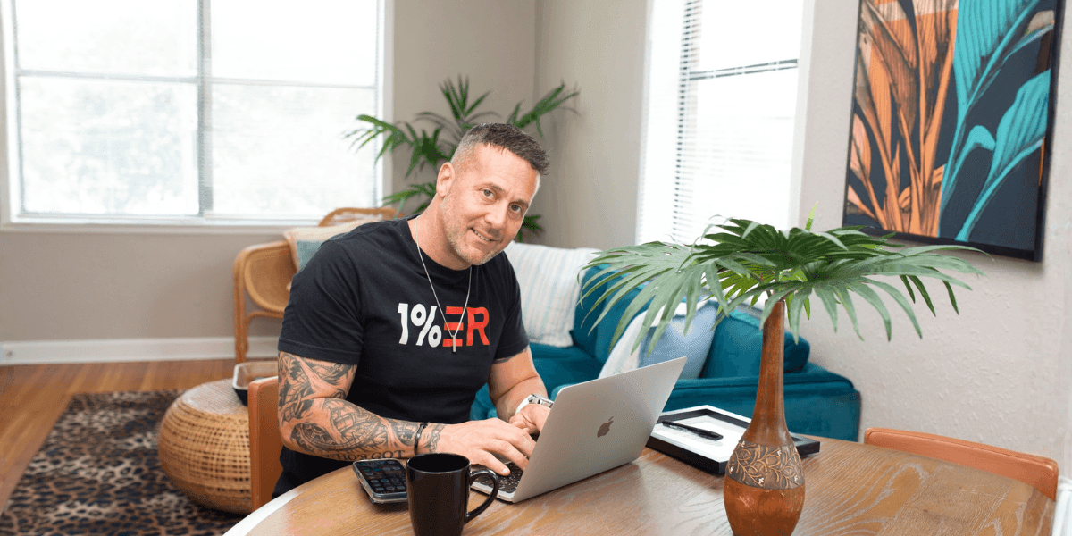 Mike working on a laptop at a table in a bright room with plants and colorful artwork.